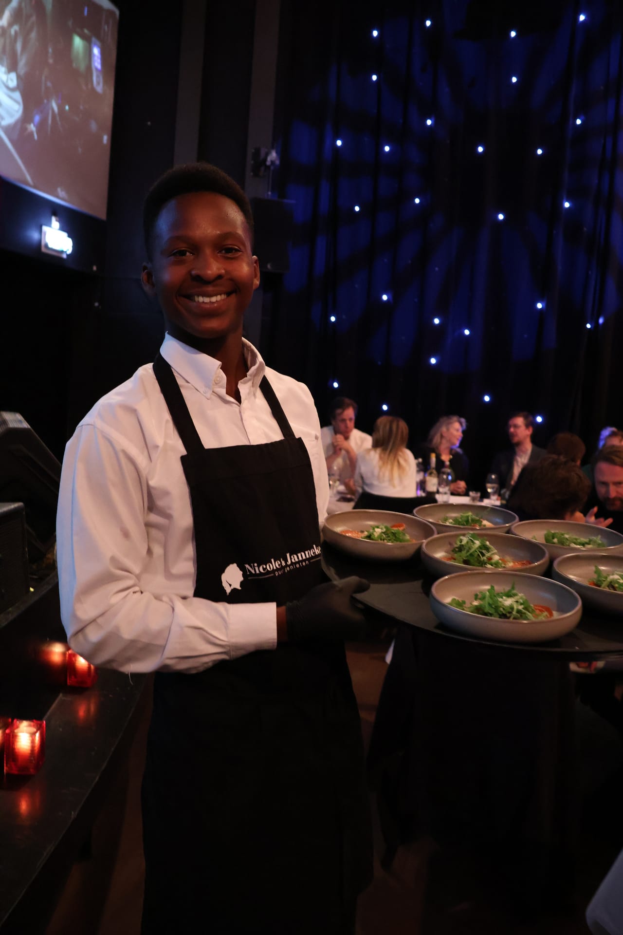 Lachend teamlid met een dienblad vol gerechten tijdens een diner op locatie